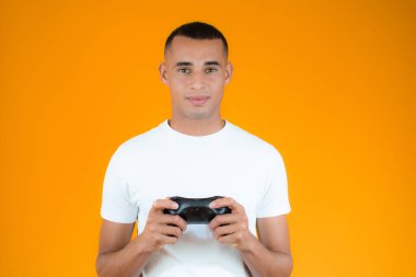 Neşeli genç adam konsolu çalıyor, turuncu arka planda joystick..