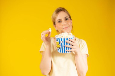 Sarı arka planda izole edilmiş patlamış mısır yiyen genç kadın.