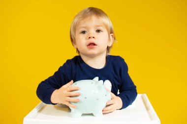 Beyaz erkek bebek, sarı arka planda domuz kumbarası tutuyor.