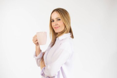 Genç, gülümseyen bir kadın izole edilmiş beyaz arka planda bir fincan sıcak kahve içiyor.