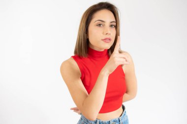 Güzel ve genç bir kadının portresi izole edilmiş beyaz arka planda duruyor ve parmakları dudaklarında sessiz olmak istiyor. Sessizlik ve gizli konsept.