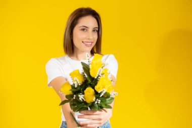 Sarı arka planda çiçekleri tutan gülümseyen kadın.