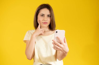 Sarı arka planda cep telefonu tutan düşünceli sıradan bir kadının portresi