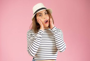 Oldukça şaşırmış genç bir kadının yakın plan portresi ağzı açık, avuçları açık, pembe arka planda izole bir şekilde duruyor.