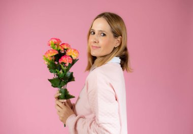 Sevgililer günü, romantizm, kutlama ve güzellik konsepti. Çekici, zarif ve kadınsı genç bir kadın elinde güzel bir buket çiçek tutarak neşeyle gülüyor, pembe bir arka plan.