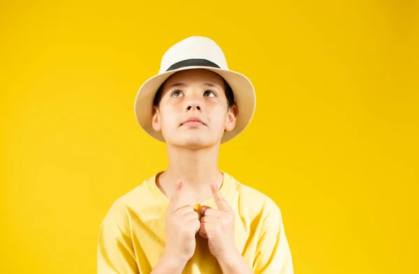 A little boy in a yellow shirt and straw hat on a yellow background. The gaze is directed at the camera.the concept of recreation and tourism.In the school holidays.