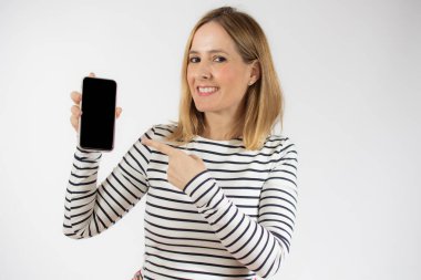 Beyaz arka planda tek başına dururken boş cep telefonu gösteren gülümseyen genç bir kadının portresi