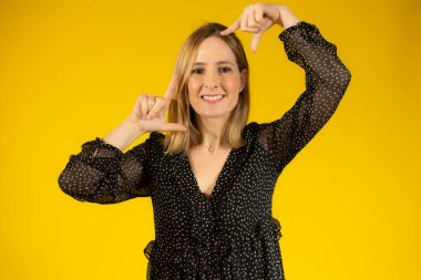 Mutlu kadın sarı arka planda parmakları izole bir çerçeve yapıyor.
