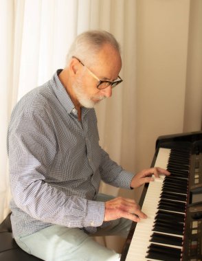 İşten emekli olduktan sonra evinin oturma odasında piyano çalmaya çalışan bir adam..