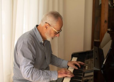 İşten emekli olduktan sonra evinin oturma odasında piyano çalmaya çalışan bir adam..