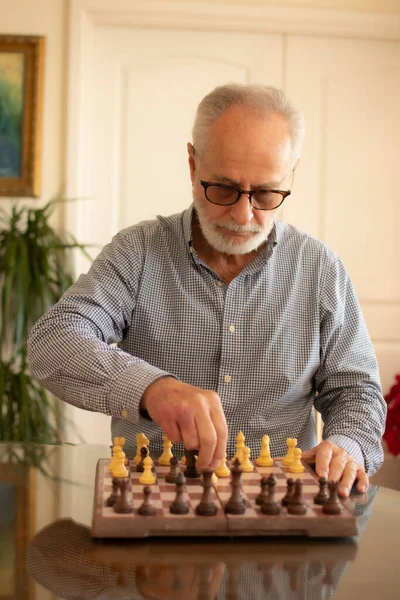Bearded senior man pensive playing chess in his living room