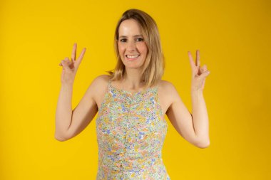 Arka planda kalmış genç bir kadın gülümsüyor ve zafer işareti gösteriyor.