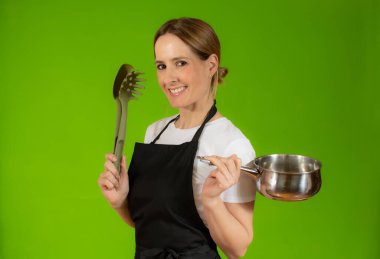 Mutfak aletlerini yeşil arka planda tutan beyaz bir kadın.