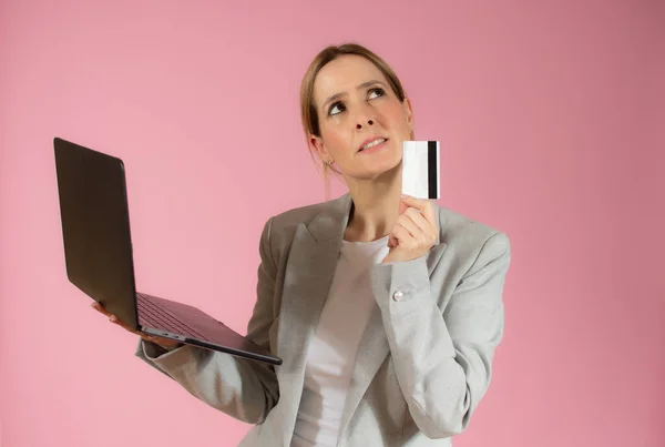 Young business woman holding laptop computer and credit card over pink background