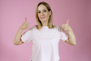 Gülümseyen güzel bir genç kadın pembe arka planda baş parmak gösteriyor.