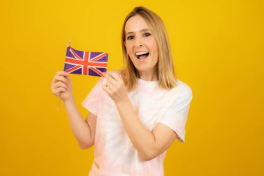 Sarı arka planda Büyük Britanya bayrağı taşıyan mutlu kadın..