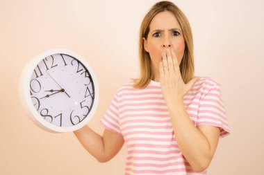 Beyaz arka planda büyük bir saat tutan genç, şaşkın bir kadın.