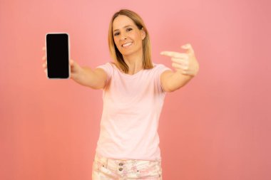 Beautiful young smiling woman showing mobile phone isolated over pink background.