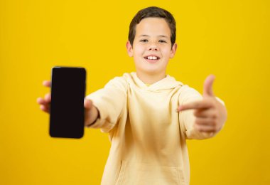 Beyaz çocuk sarı arka planda izole edilmiş bir telefonla iyi niyet gösterisi yapıyor.