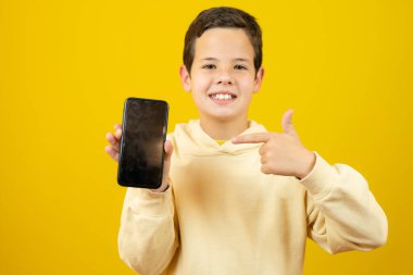 Beyaz çocuk sarı arka planda izole edilmiş bir telefonla iyi niyet gösterisi yapıyor.