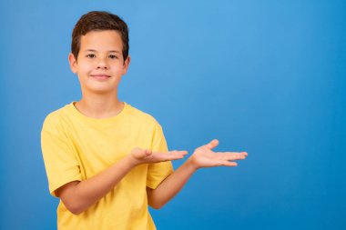 Beautiful young boy over isolated blue background smiling, showing and pointing something that is on his fingers