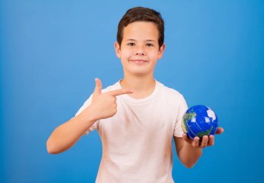 Portrait of a young caucasian boy holding a world globe over blue background