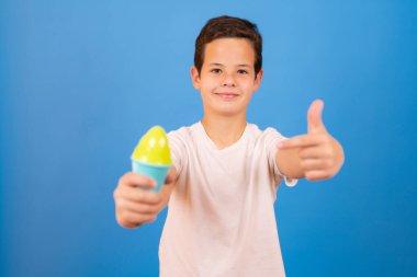 Happy boy holding ice cream cone over blue background
