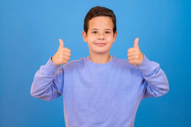 Portrait of cheerful boy with good idea - isolated over blue background. 10 year old kid pointing finger up. Child points by fingers upward. Cheerful boy shows something