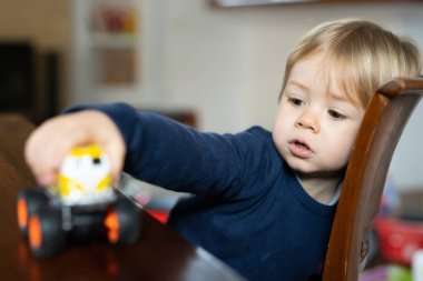 Küçük sevimli çocuk oturma odasında oturup oyuncakla oynuyor.