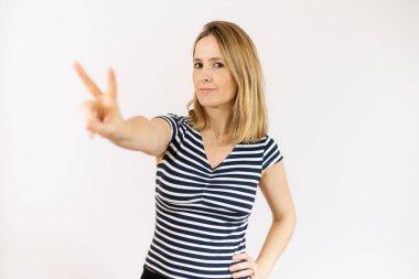 Sarışın kadın, izole edilmiş arka planda gülümsüyor ve zafer işareti gösteriyor.