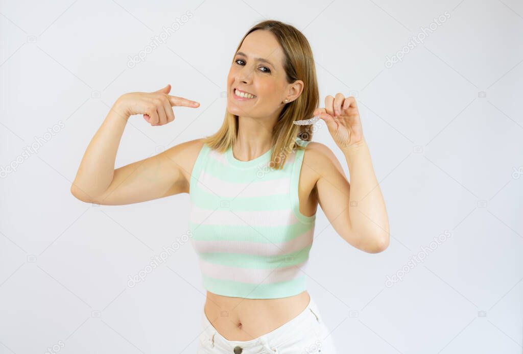 Young beautiful woman holding an invisible aligner braces against white studio background smiling and showing her perfect white teeth. Dental healthcare concept.