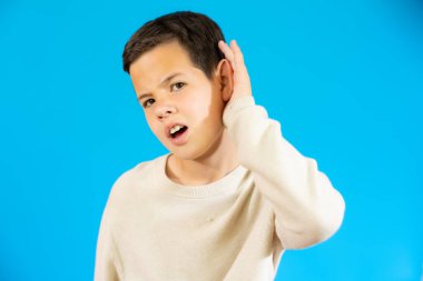 Little child making listening gesture isolated over blue background.