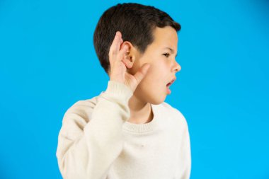 Little child making listening gesture isolated over blue background.