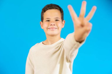 Smiling child in casual sweater counting three isolated over blue background