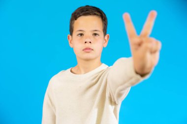 Cute boy in casual sweater showing victory sign isolated over blue background