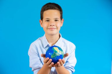 School boy holding a world globe isolated over blue background
