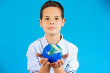 Closeup portrait of school boy holding a world globe isolated over blue background