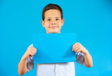 Cute boy showing a blue blank paper isolated over blue background