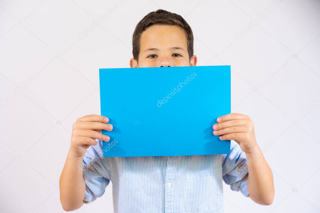 Cute boy holding blue blank paper covering mouth isolated over white background