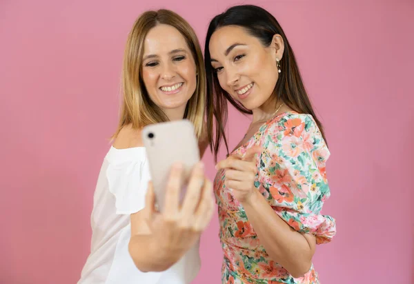 Två Vänner Som Använder Mobiltelefonen Över Rosa Bakgrund — Stockfoto