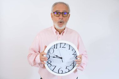 Saati işaret eden bir emeklinin portresi beyaz arka planda izole edilmiş pembe bir gömlek giy.