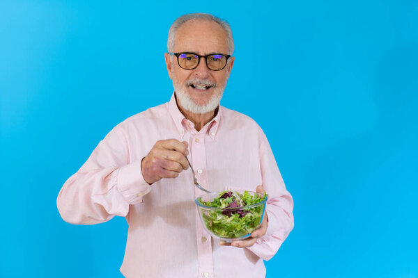Весёлый старшеклассник держит миску с салатом и смотрит на камеру на синем фоне