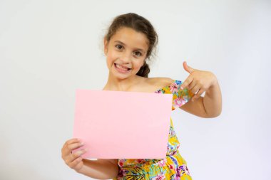 Gülümseyen küçük kız beyaz arka planda boş pembe bir tahta tutuyor..
