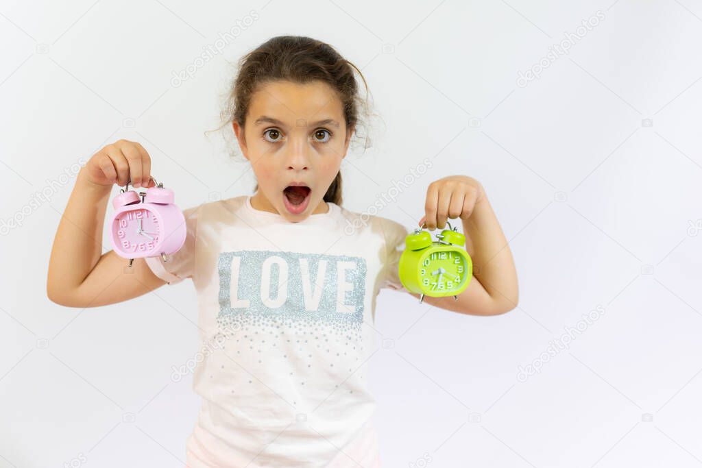 Portrait of little girl holding two alarm clocks isolated on white background