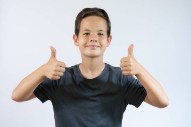 Neşeli gülümseyen küçük çocuk beyaz arka planda duruyor ve baş parmağını kaldırıyor.