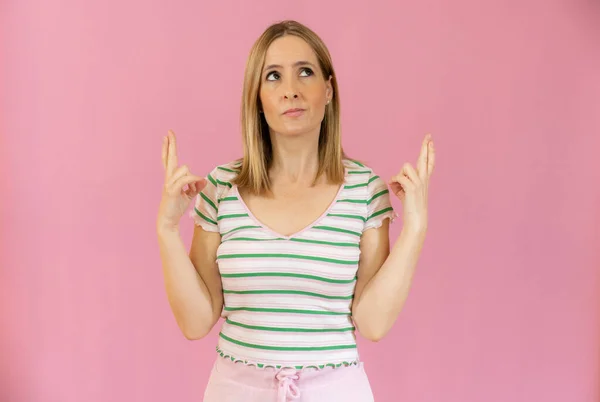 Intrigued Woman Shirt Praying Crossed Fingers Looking Away Pink Background — Stock Photo, Image