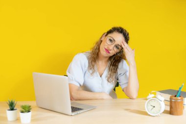 Endişeli kadın sarı arka planda bilgisayar bilgisayarı üzerinde çalışıyor..