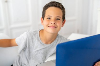 Yatak odasında dizüstü bilgisayar kullanarak gülümseyen genç çocuk.