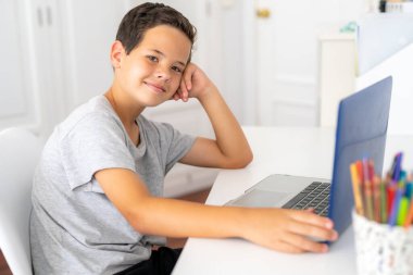 Yatak odasında dizüstü bilgisayar kullanarak gülümseyen genç çocuk.