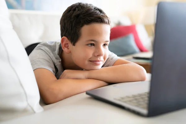 Picture of cute boy using laptop computer while lies on sofa at home.